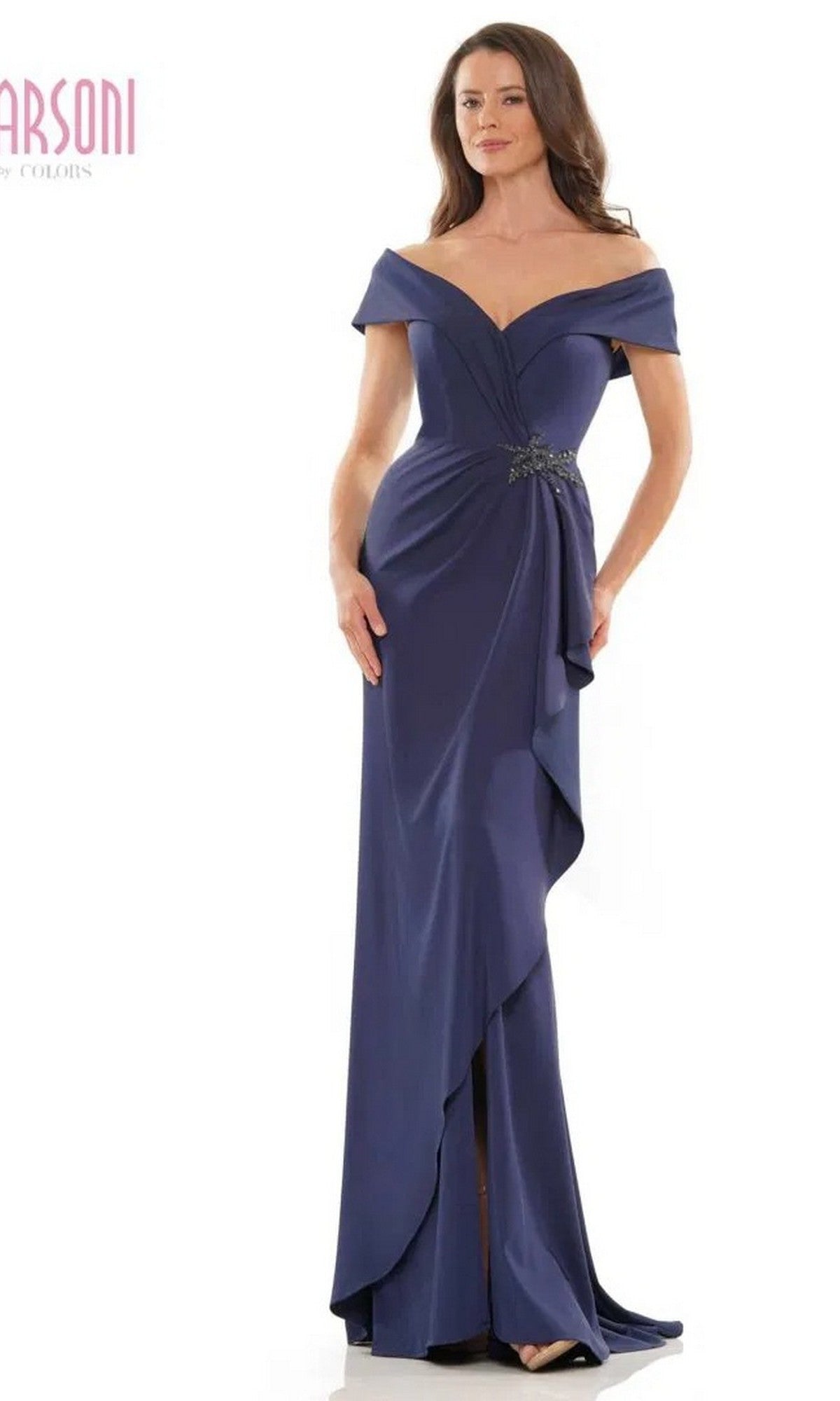 A woman wears the Marsoni MV1180, a long formal navy evening dress featuring an off-the-shoulder neckline, beaded waistline, and draped asymmetrical skirt.